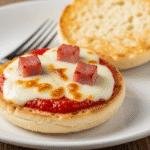 একটি ইংলিশ মাফিনের অর্ধেক অংশে তৈরি দ্রুত ব্রেকফাস্ট পিৎজা, উপরে গলানো মোজারেলা পনির, টমেটো সস এবং রান্না করা হ্যাম।