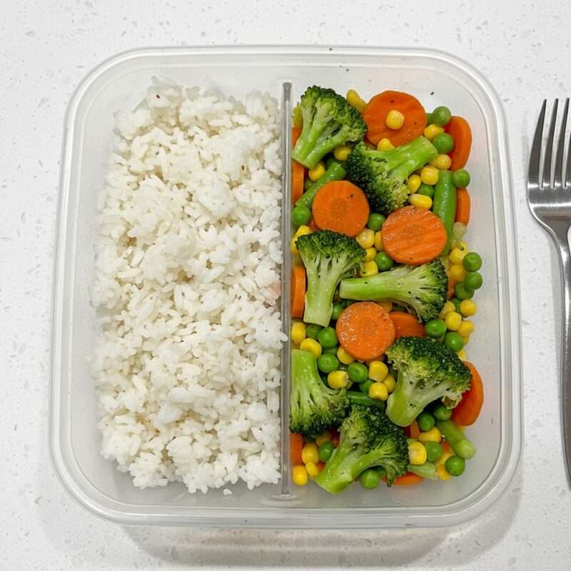 A practical, divided meal container showing quick, microwaved steamed vegetables and rice for healthy, fast fuel