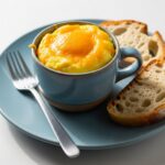 Finished microwave egg mug breakfast with melted cheese on top, served with a side of toast on a blue plate.